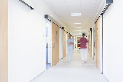 Ein Krankenhausflur, den zwei Pflegekräfte schnell entlanglaufen 