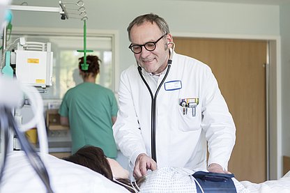 Ein Arzt mit Stethoskop hört eine im Bett liegende Patientin ab